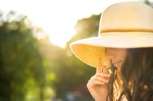 Woman shielding face with sun hat, soft golden tones