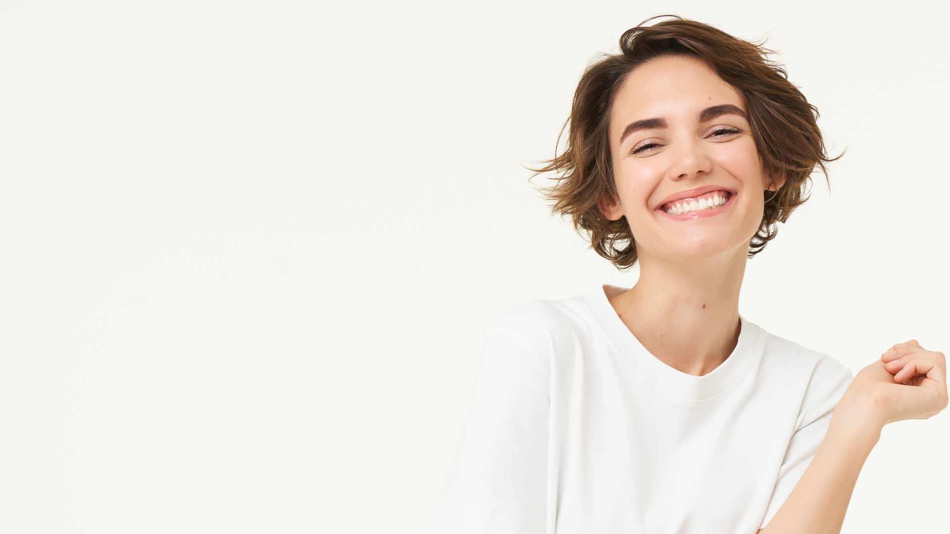 Close-up of a smiling young woman with short brown hair wearing a white t-shirt.
