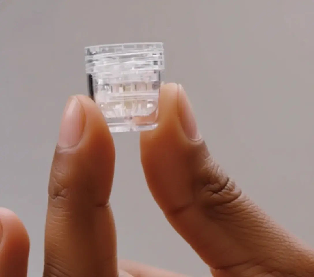 The tip of the petal microneedling device is held between fingers against a neutral background